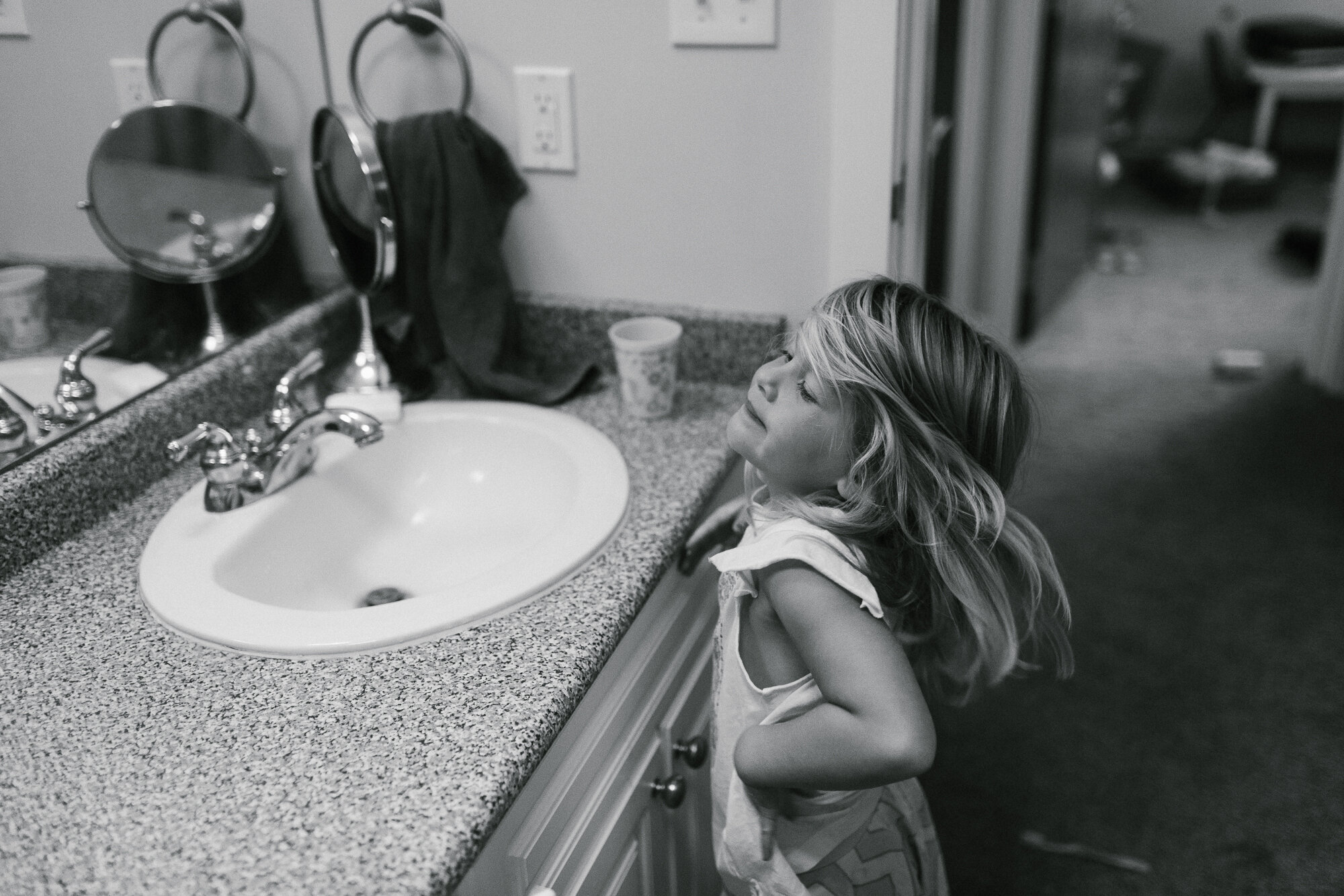 black and white photo of young girl being playful in the bathroom