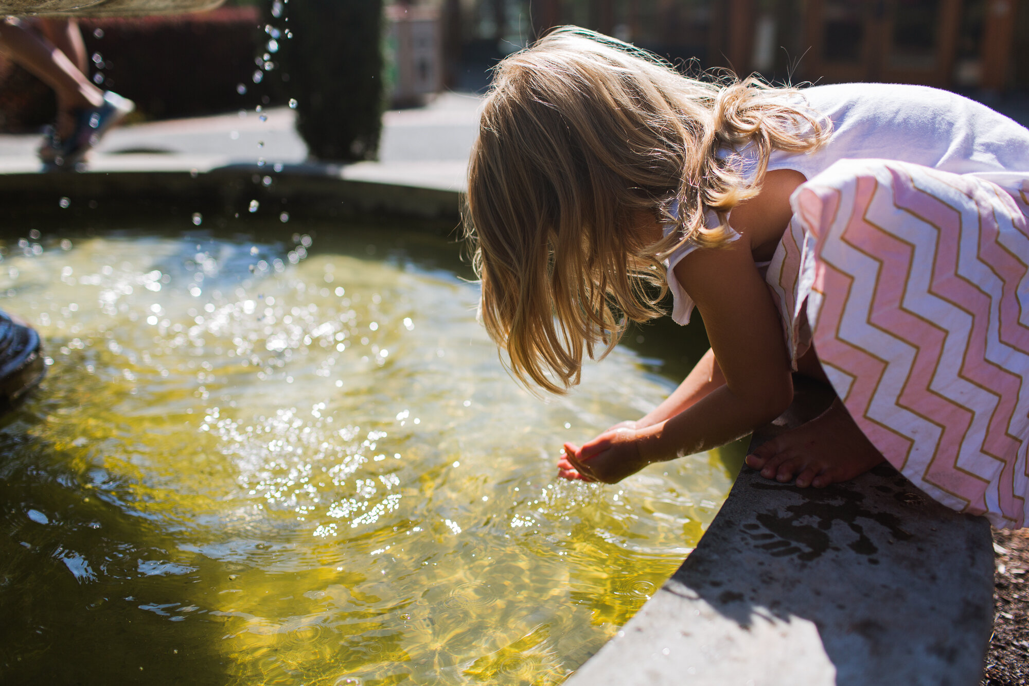 sunny summer photo of girl in dress playing in a fountain