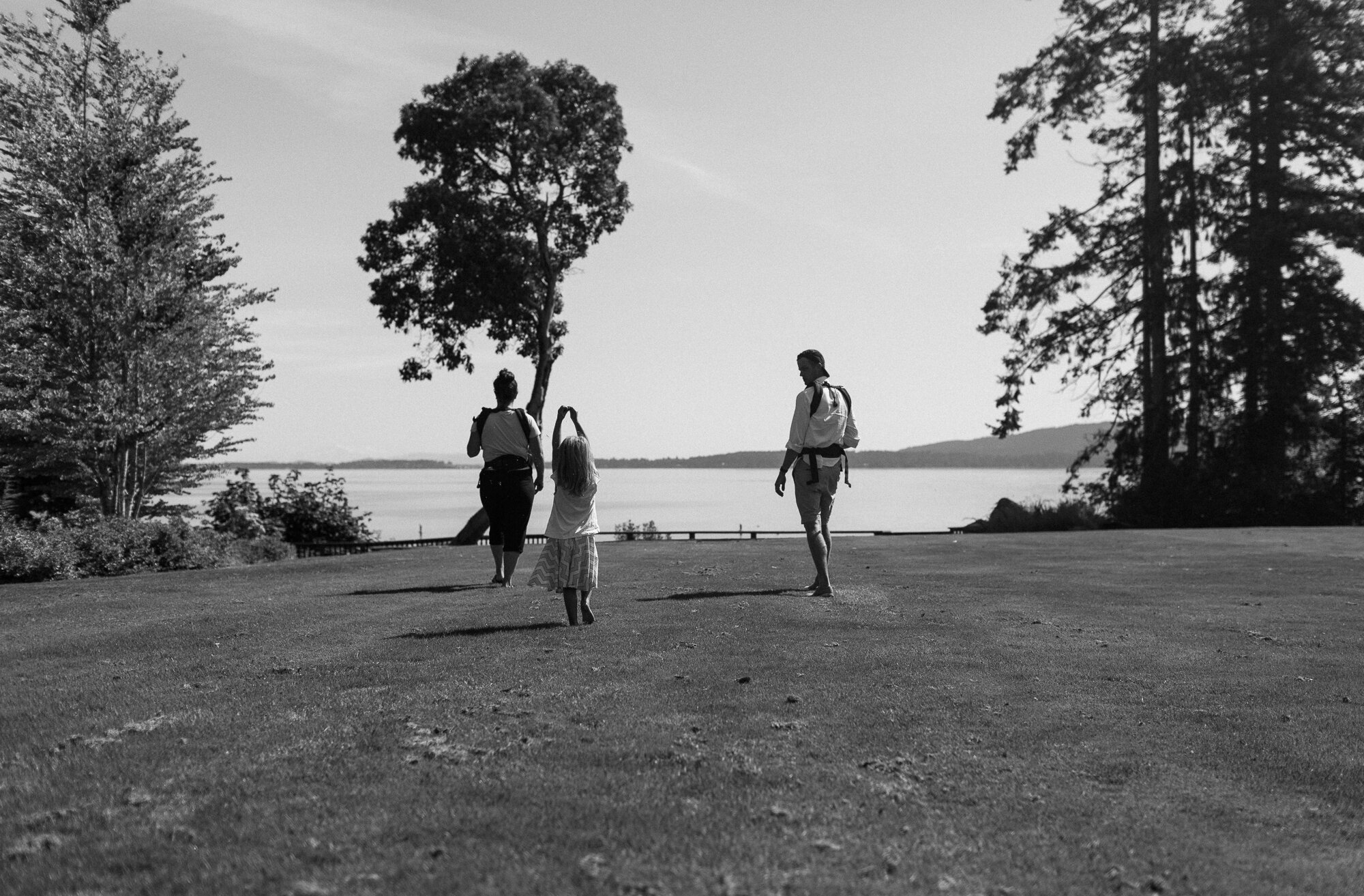 black and white long shot of family playing on the grass with ocean and trees