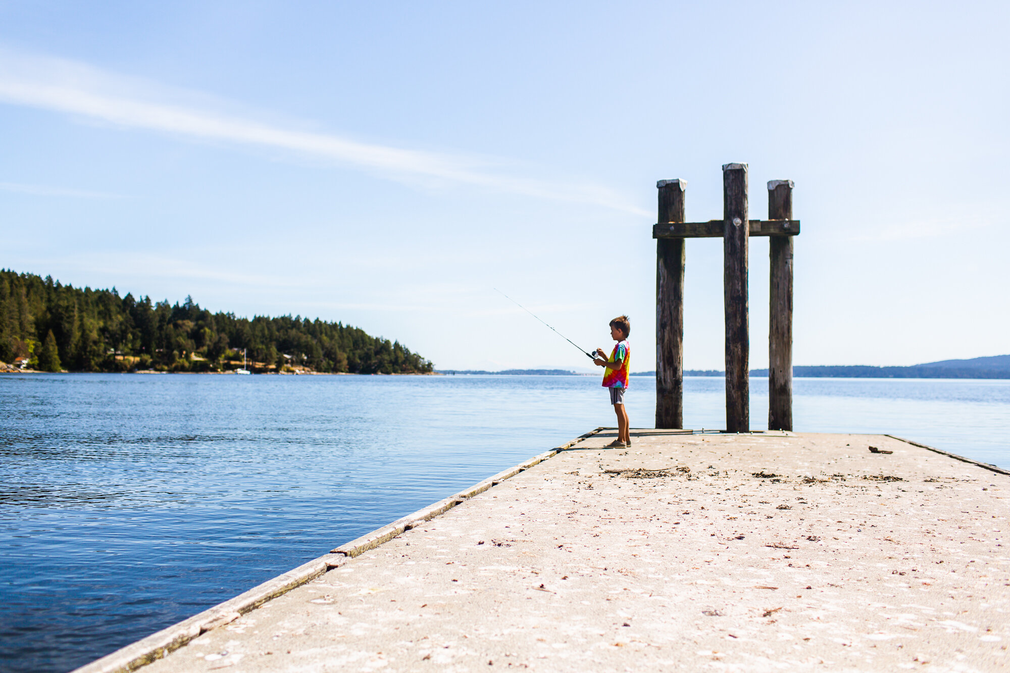 beautiful view of a boy standing on a dock fishing in Mill Bay, BC