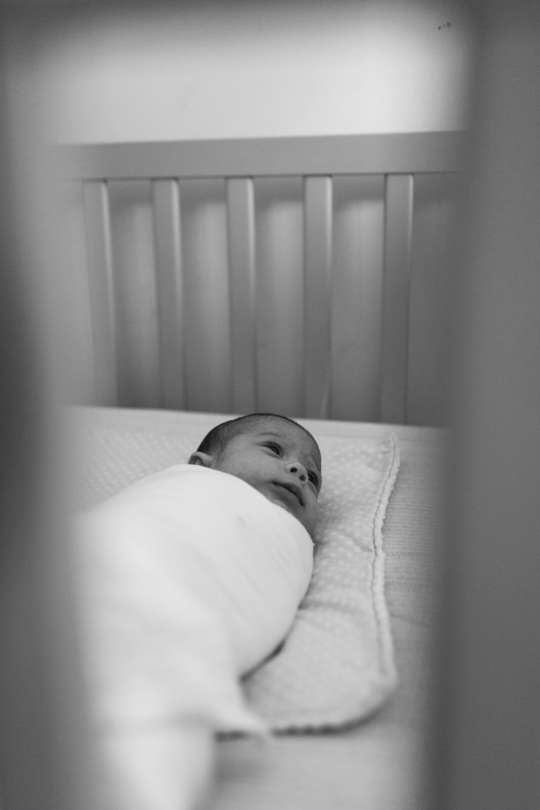black and white photo of newborn baby swaddled in crib