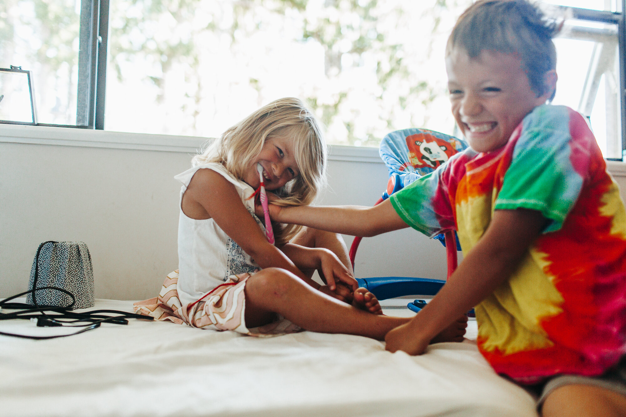 Brother and sister laughing and tickling during a light-filled in home family photography session