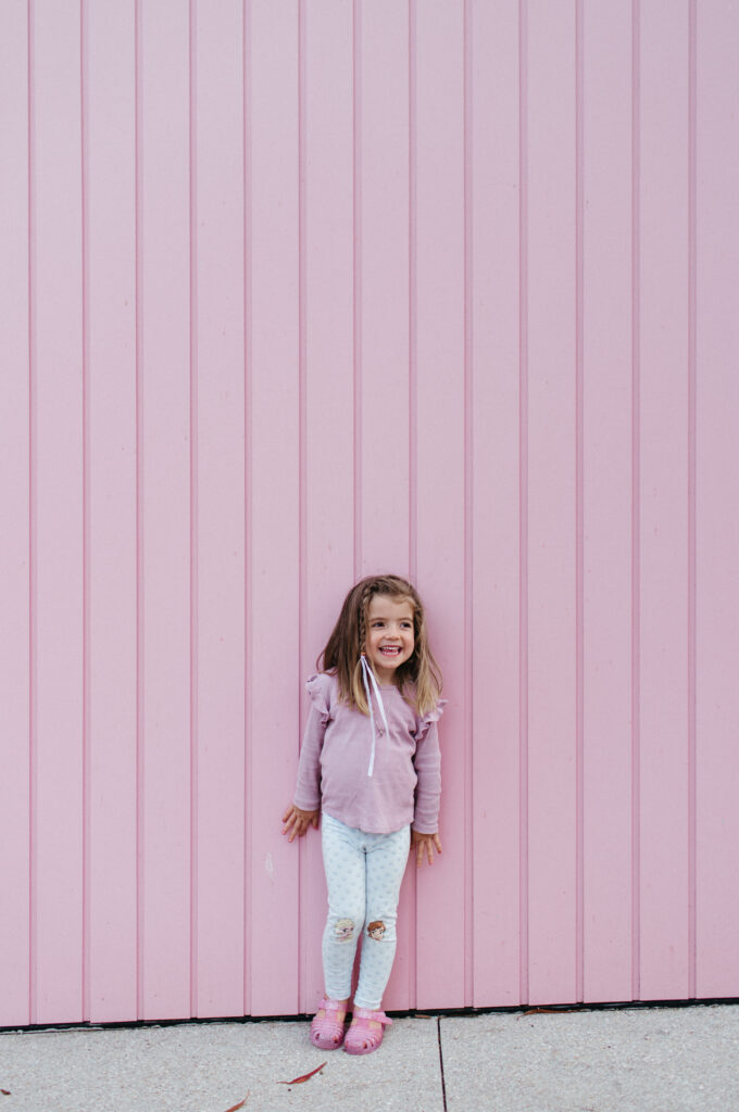 Little girl laughing in front of pink wall