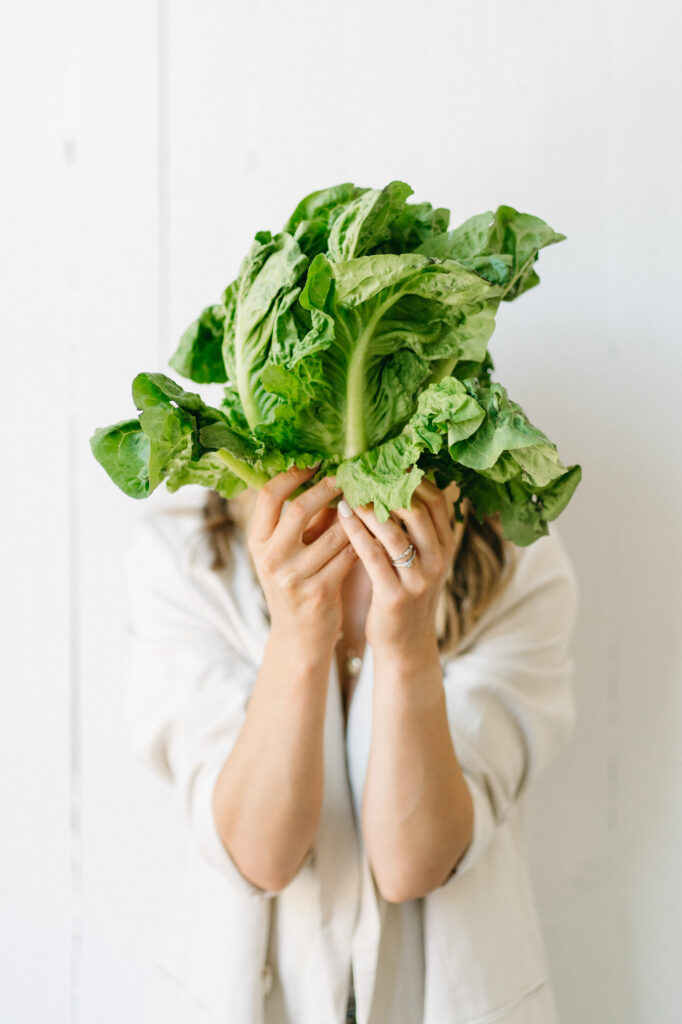 Woman holds up a lettuce in front of her face.