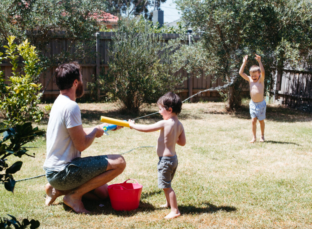 Dad squirts his kid in the backyard with a water pistol on a hot day.