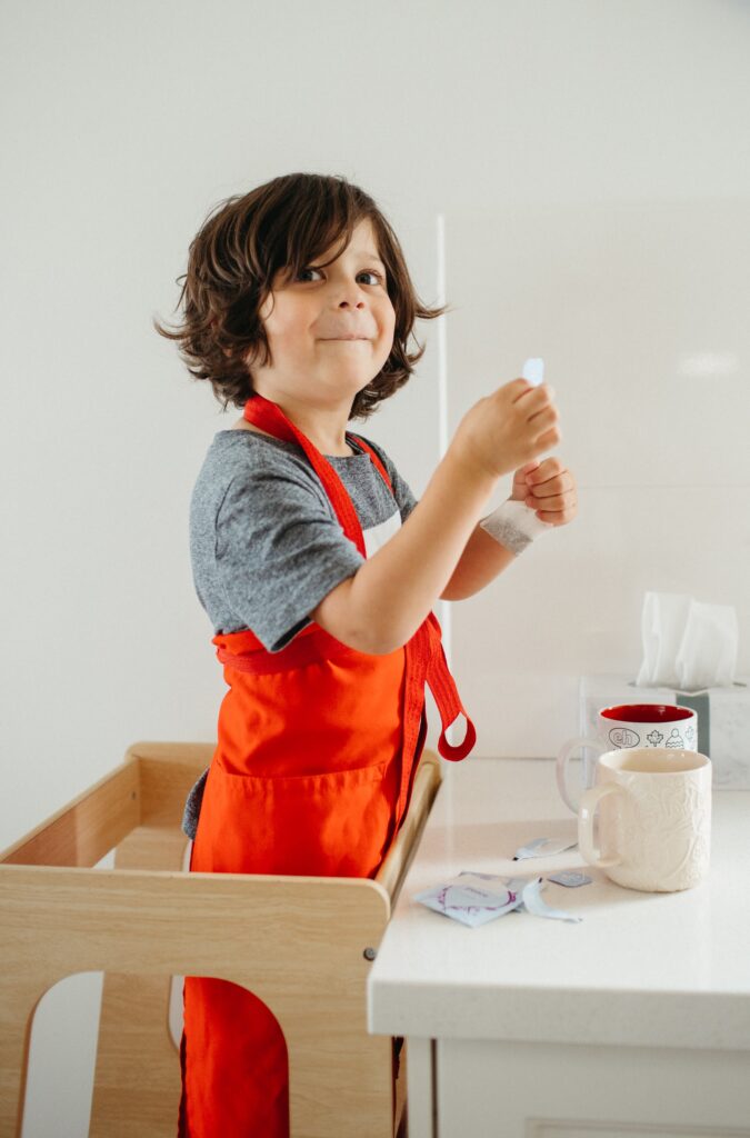 Cute young boy puts on apron to do some baking and make a cup of tea.