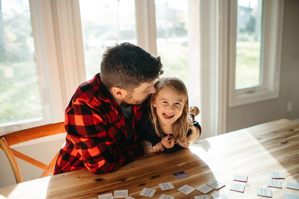 Dad plays board games with his young daughter as she laughs.