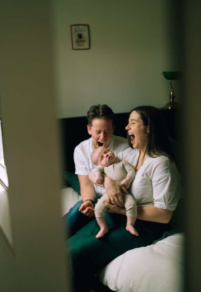 Two mums yawning with their newborn baby.