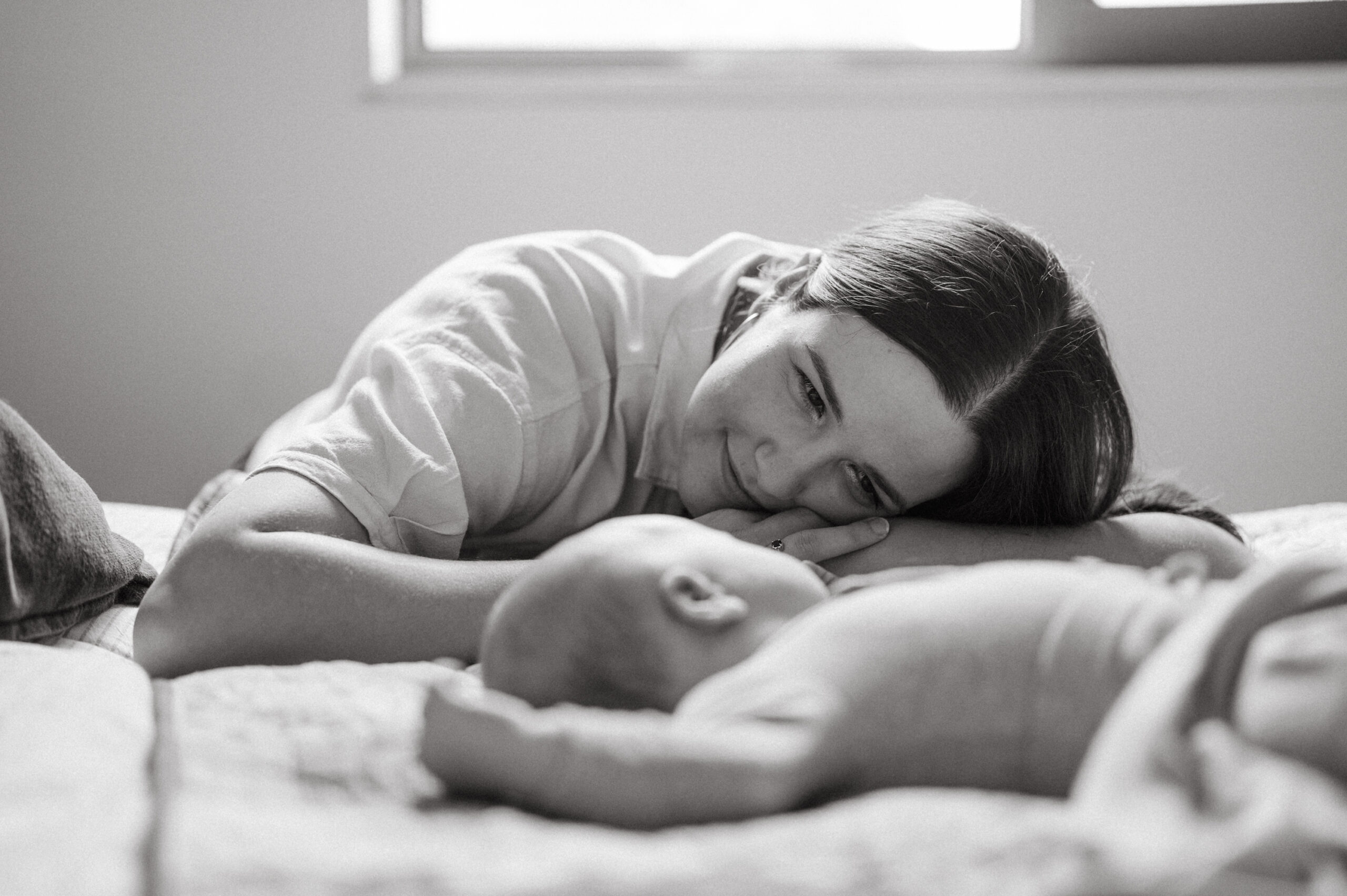 New mother looks lovingly at her newborn in a black and white photo.