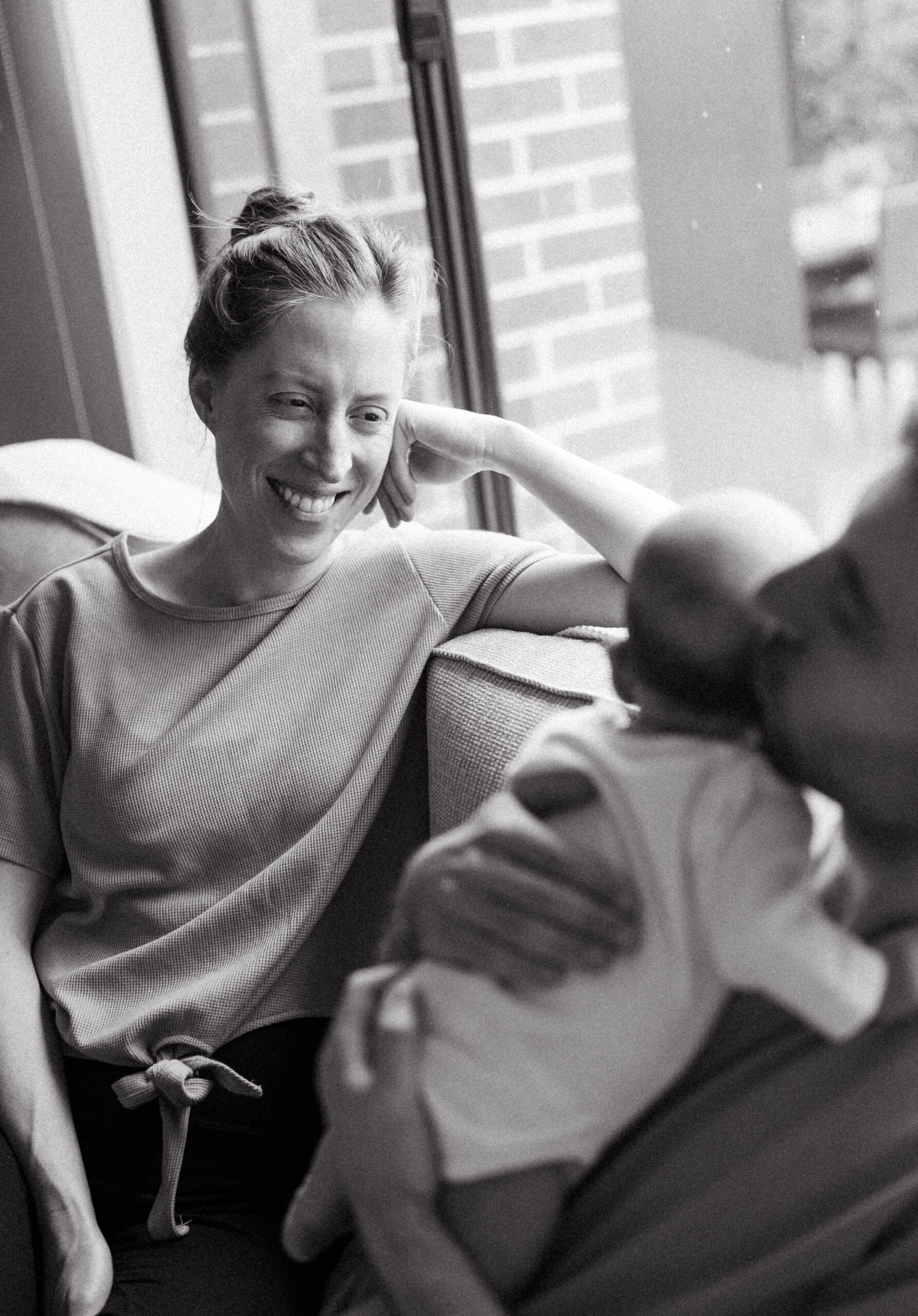black and white film photograph of a mum smiling at her partner holding their newborn baby